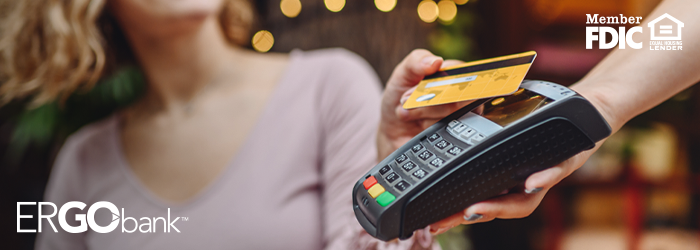 Image shows woman holding debit card to handheld payment device in an outdoor setting