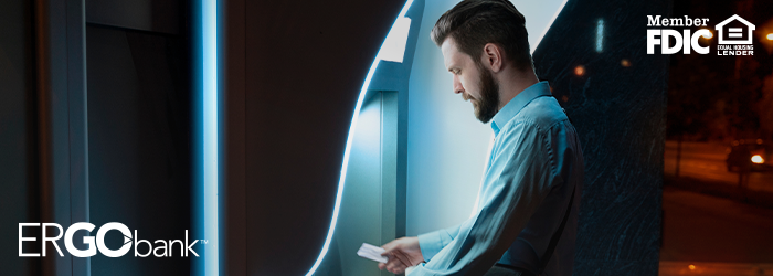 Man outside at night using an ITM with his debit card out in his hand