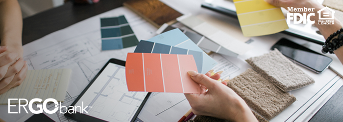 Person's hands holding paint swatches above table filled with home renovation plans