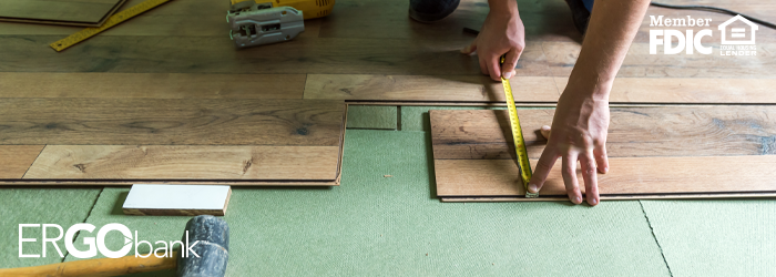 Image of person measuring wooden flooring with other tools scattered on floor