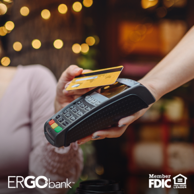 Image shows woman holding debit card to handheld payment device in an outdoor setting